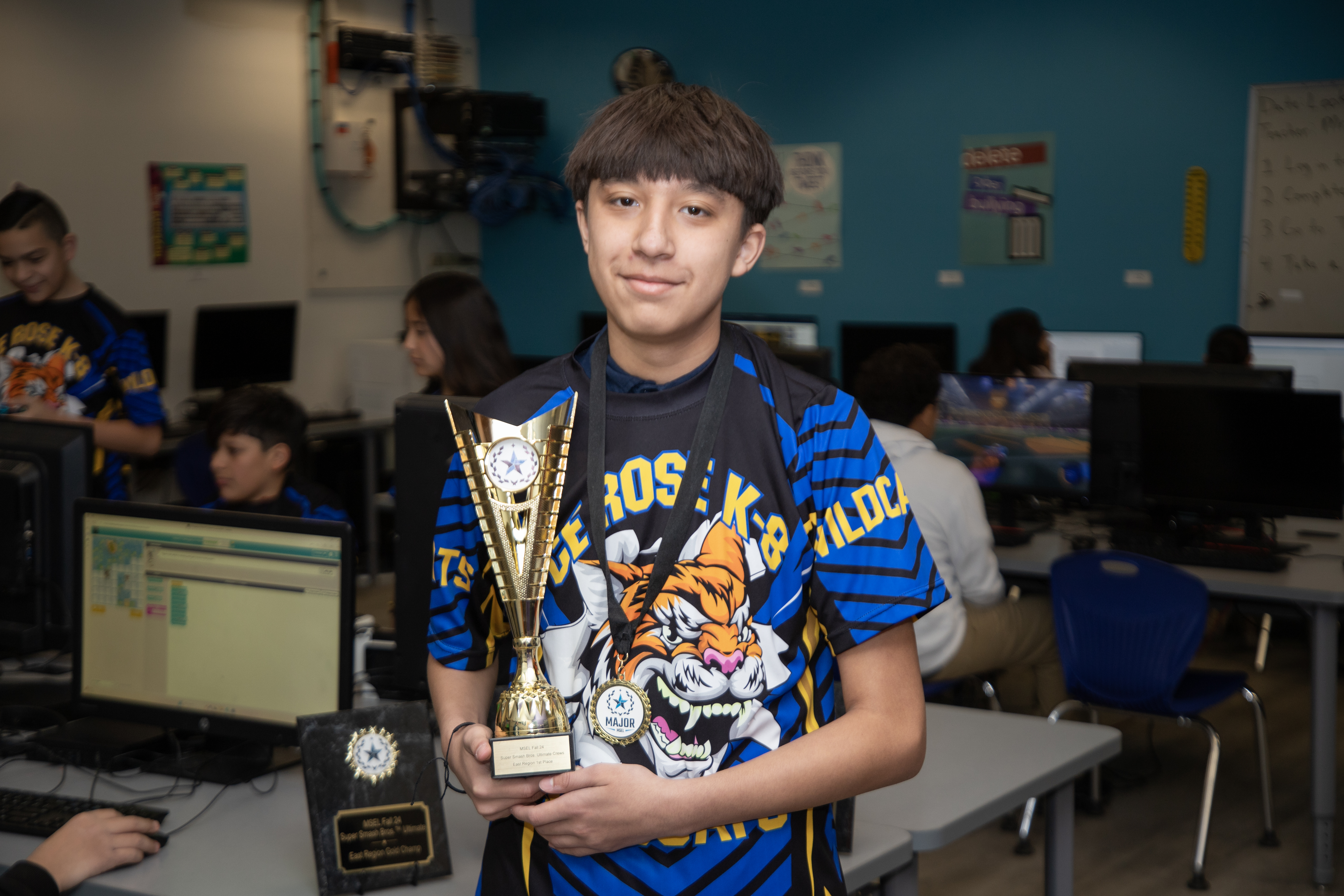 A boy in a CE Rose shirt holds up a trophy