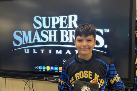 A boy in a CE Rose shirt stands in front of a Super Smash Bros screen