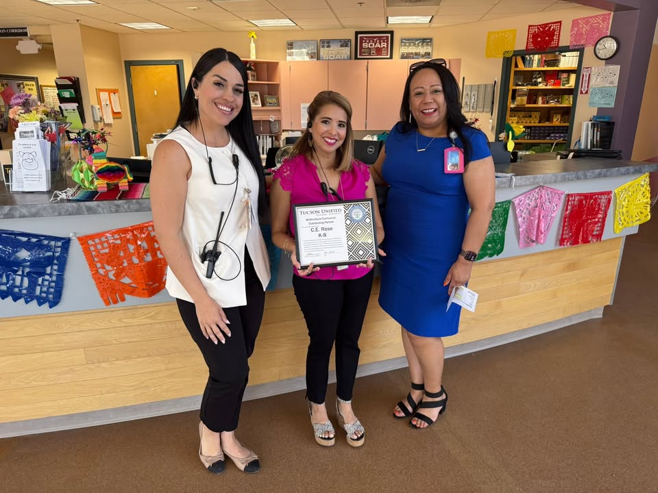 Three women smile in front of the desk in the front office