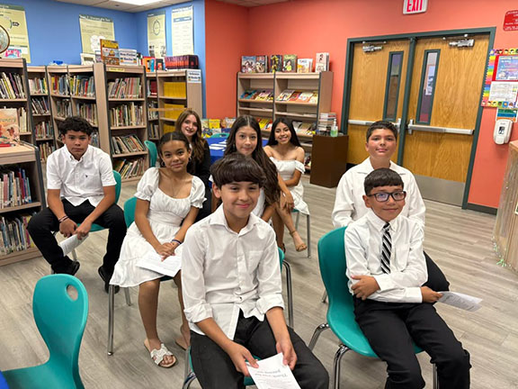 Students wearing nice clothes sit in teal chairs in the library
