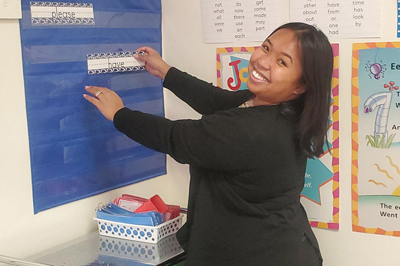 A woman in a black shirt smiles as she decorates her classroom