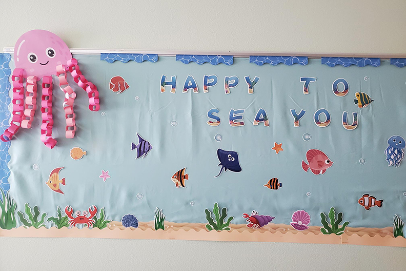An ocean themed white board decorated with sea creatures and the words Happy to Sea You