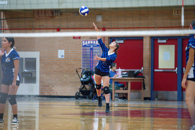 A girl in a blue striped jersey jumps up to hit the volleyball over the net