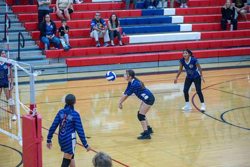 A girl in a blue striped jersey hits the volleyball over the net with both arms