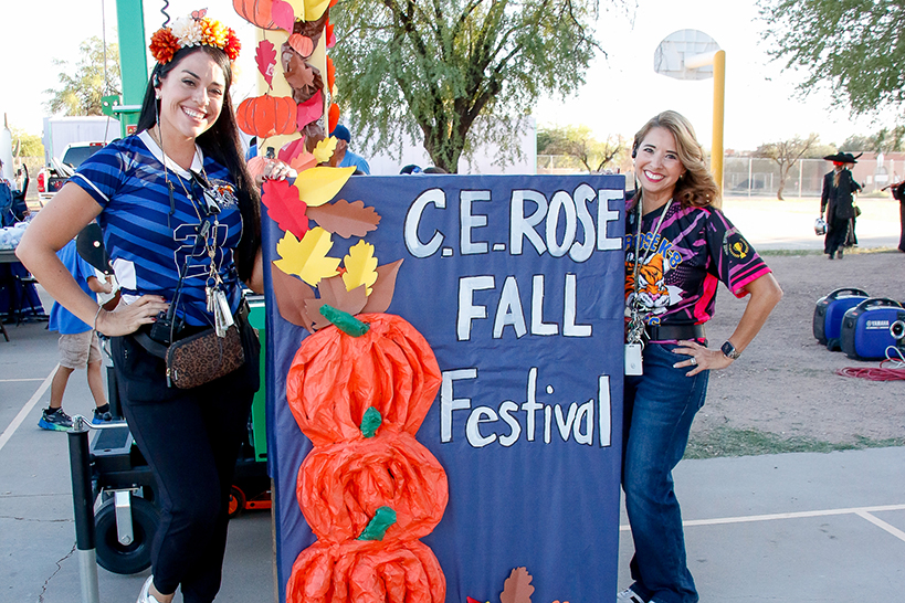 Two women smile in front of the CE Rose Fall Festival sign