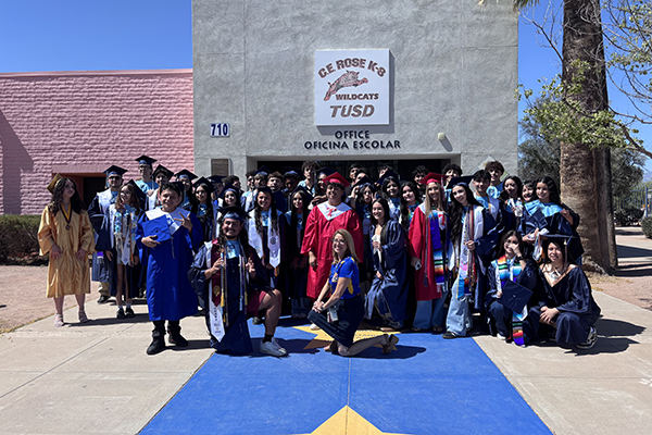 Students in their caps and gowns pose for a group photo in front of the school office