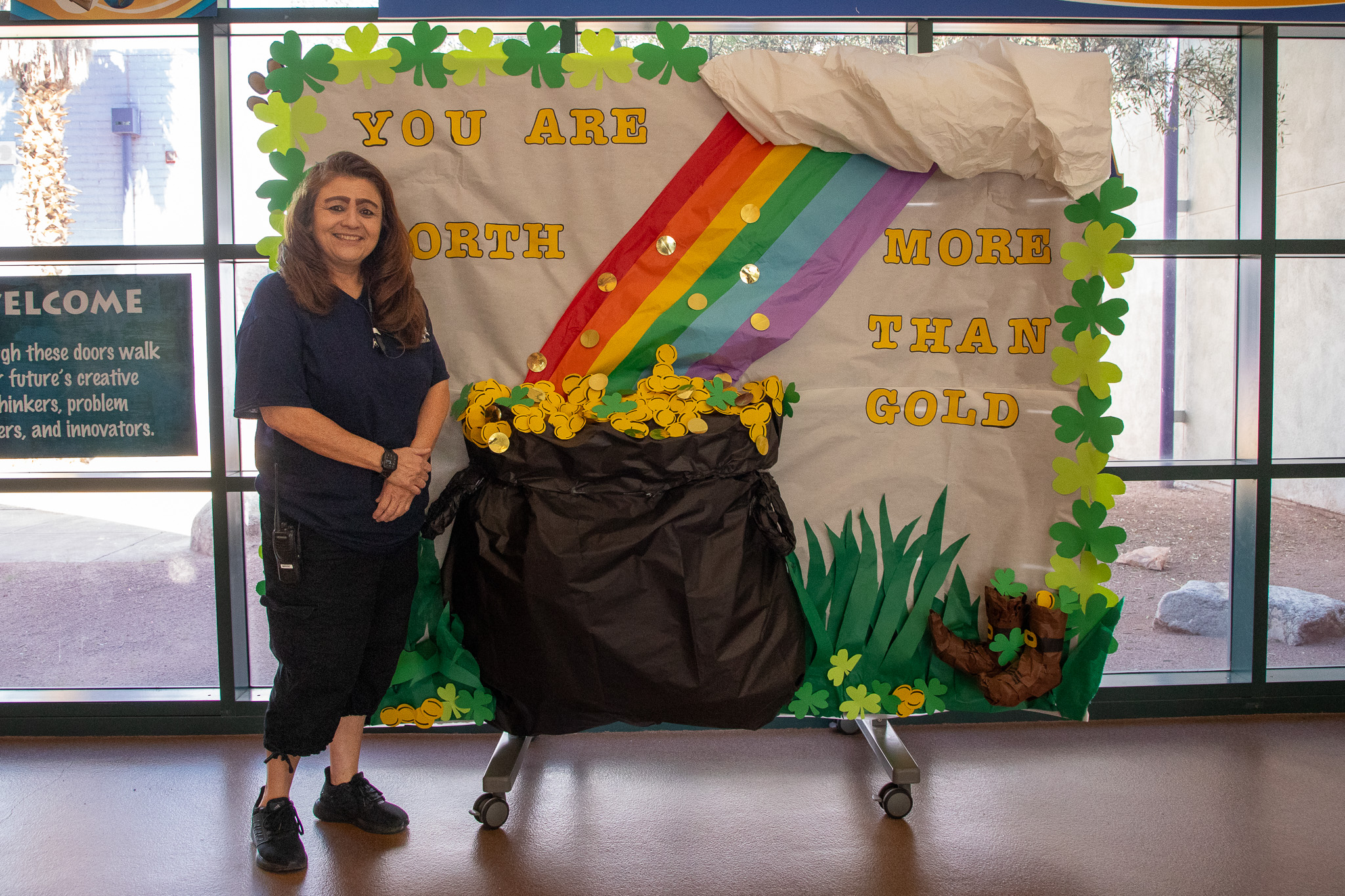 A woman stands in front of a backdrop depicting a pot of gold at the end of a rainbow