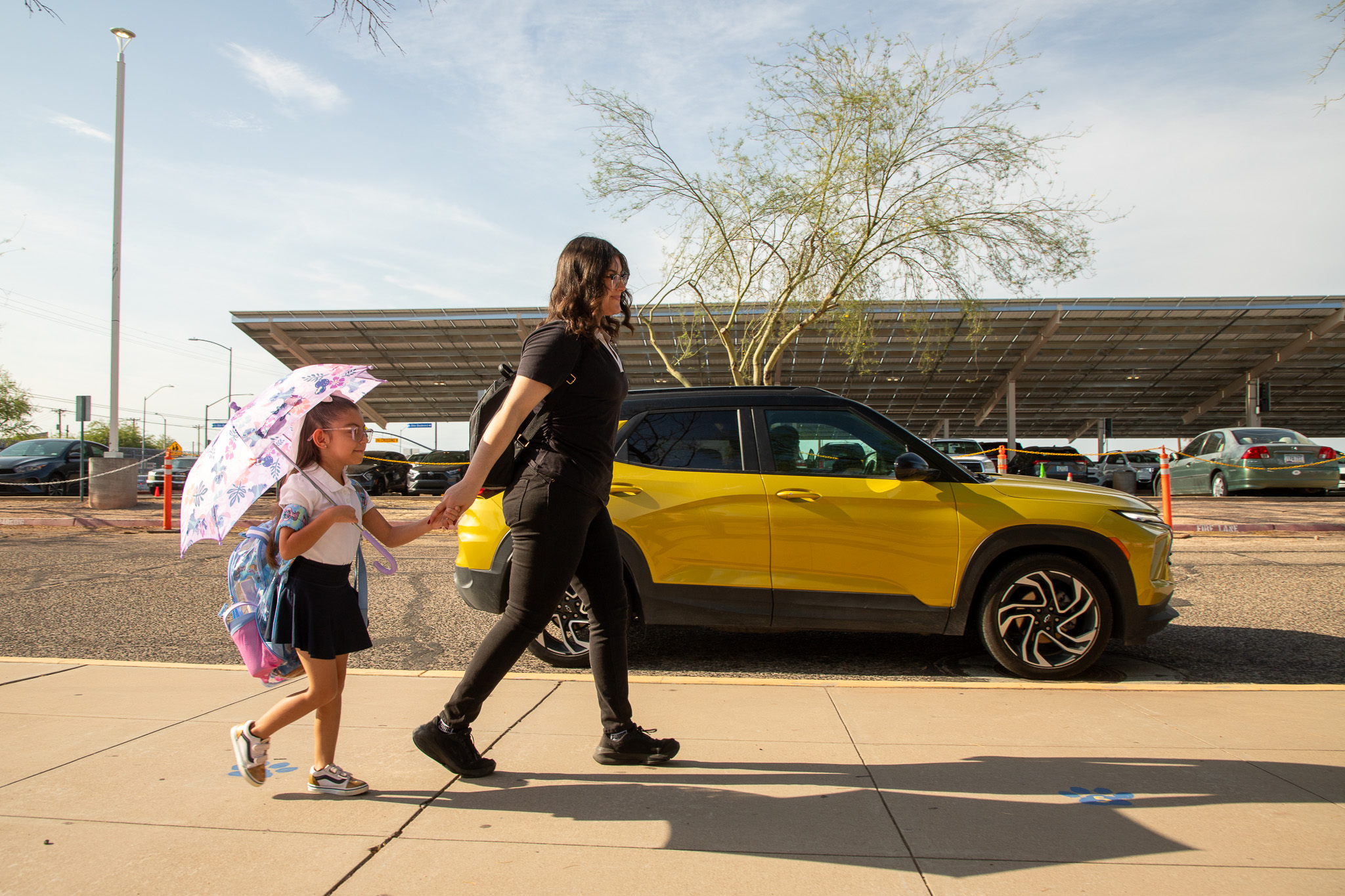 A mom walks with her young daughter in front of a yellow SUV