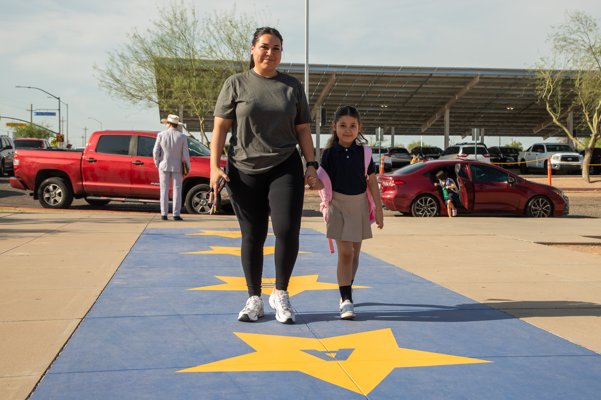 A mom and her daughter walk from the parking lot on the school's blue and yellow star sidewalk