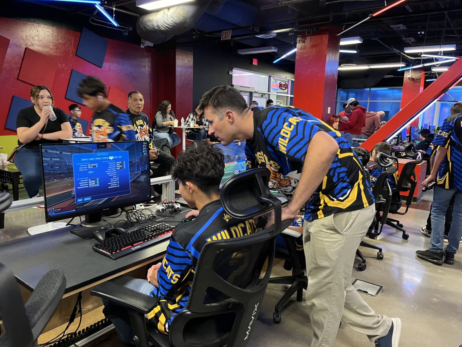 A student looks at the computer while a teacher looks over his shoulder.